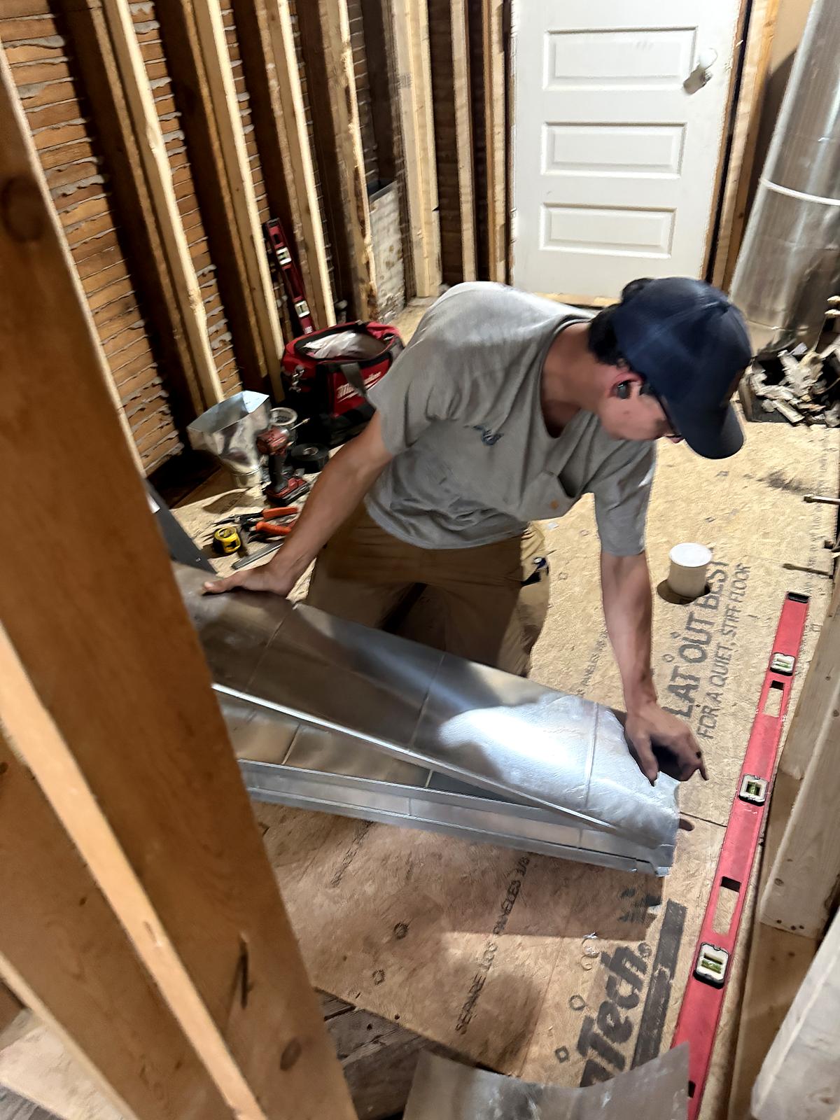 First Class technician fabricating custom sheet metal ductwork between floor joists