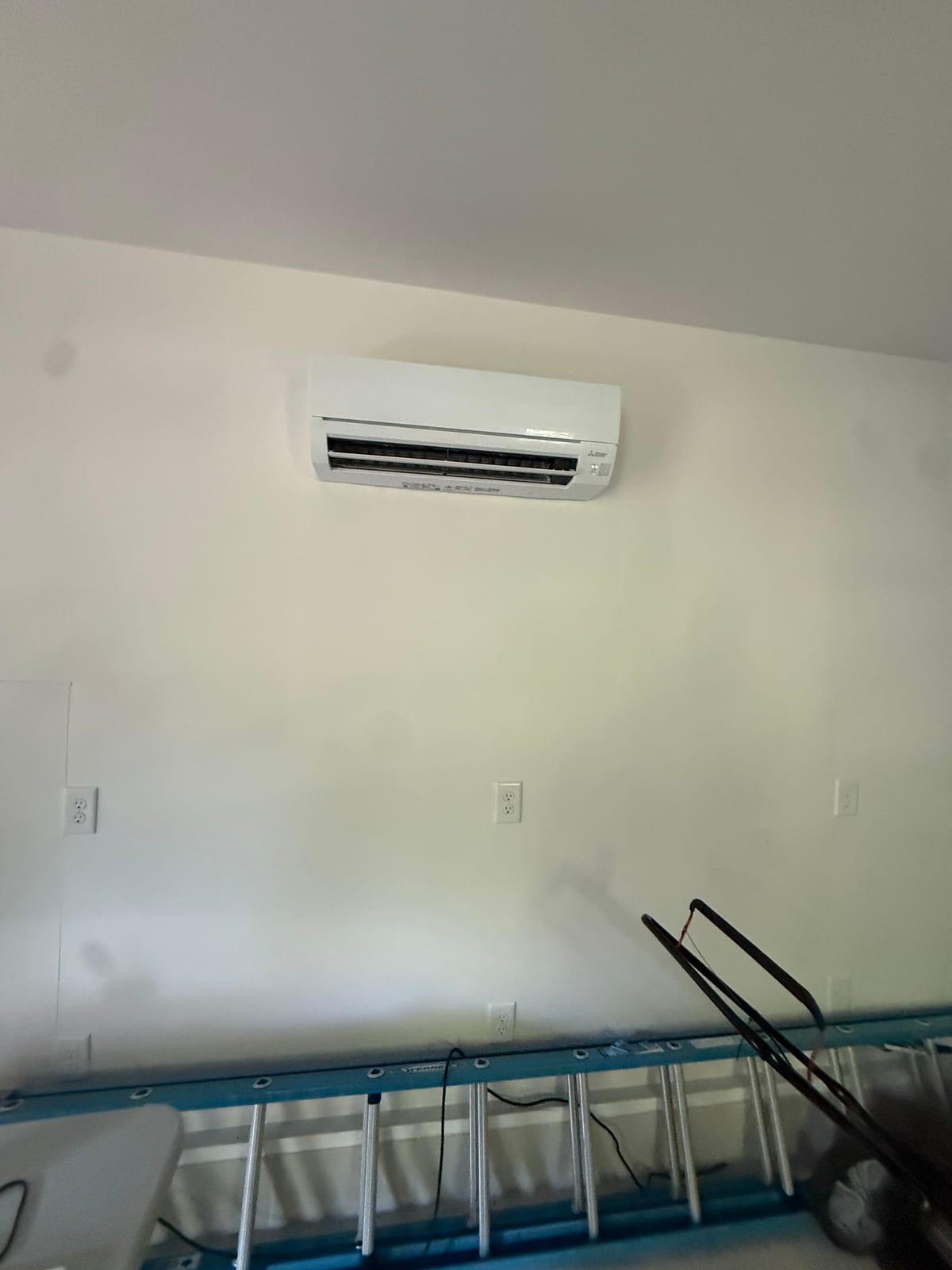 Mitsubishi wall-mounted ductless mini split indoor head installed high on a clean white wall